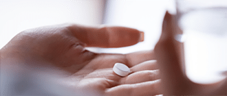 A hand holding a white pill and water.