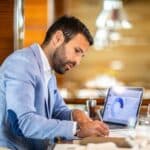 man writing at a desk with business model on his laptop