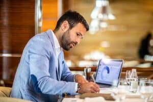 man writing at a desk with business model on his laptop