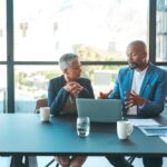business man and woman sitting at a table in front of a laptop in discussion