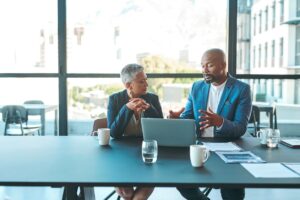 business man and woman sitting at a table in front of a laptop in discussion