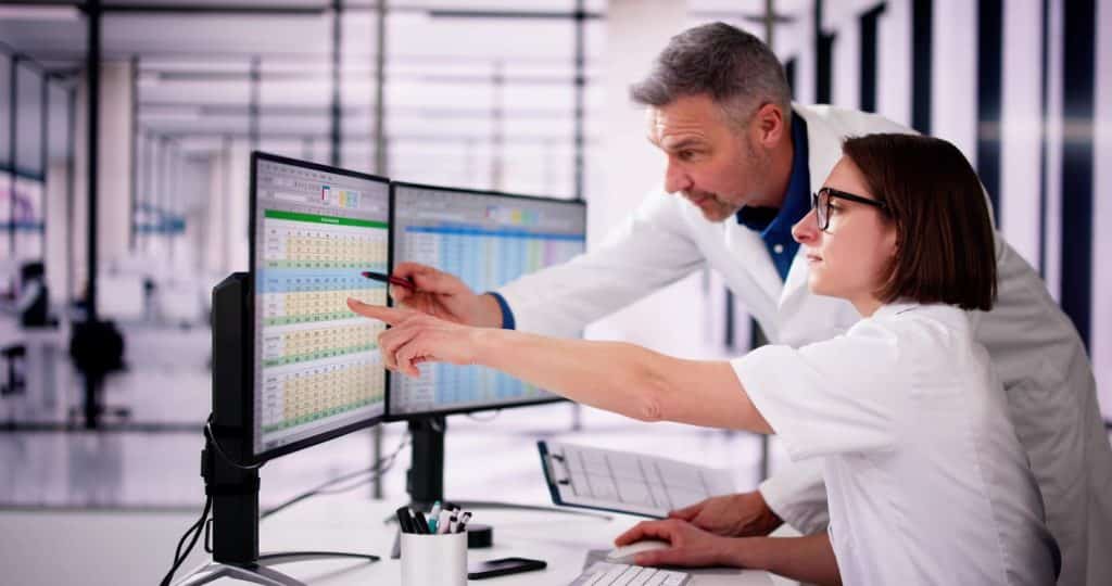 two medical employees analyzing data on computer monitors