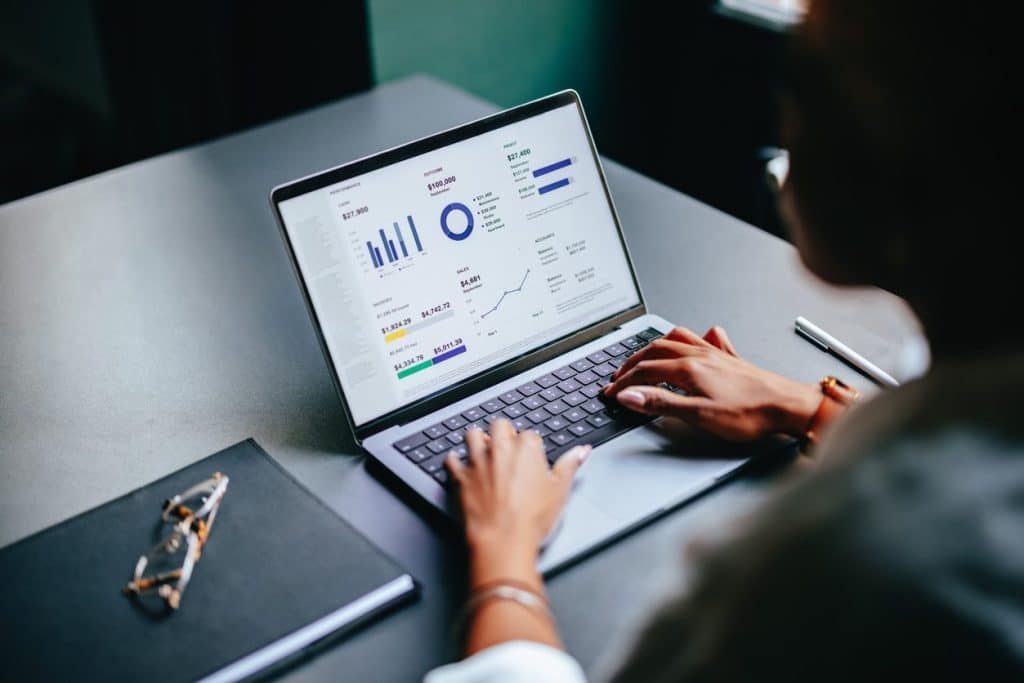 person typing on laptop with graphs on monitor