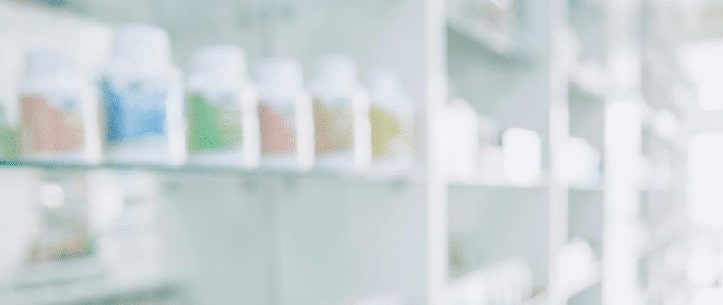 A blurred image of prescription drug bottles on pharmacy shelves.